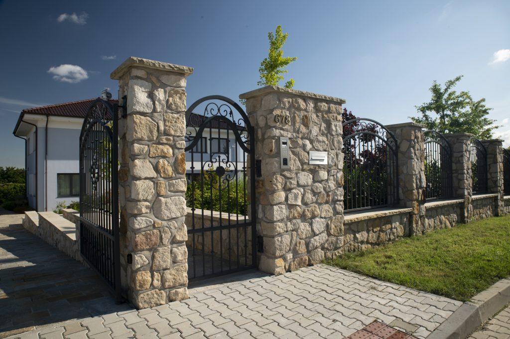 Kamenné ploty z pískovce Vyhnánov Kamenné ploty z pískovce Vyhnánov s masivními sloupky a kovanou bránou, přírodní kámen použitý na oplocení rodinného domu.