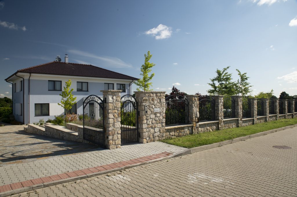 Kamenné ploty z pískovce Vyhnánov Kamenné ploty z pískovce Vyhnánov s masivními sloupky a kovanou bránou, přírodní kámen použitý na oplocení rodinného domu.
