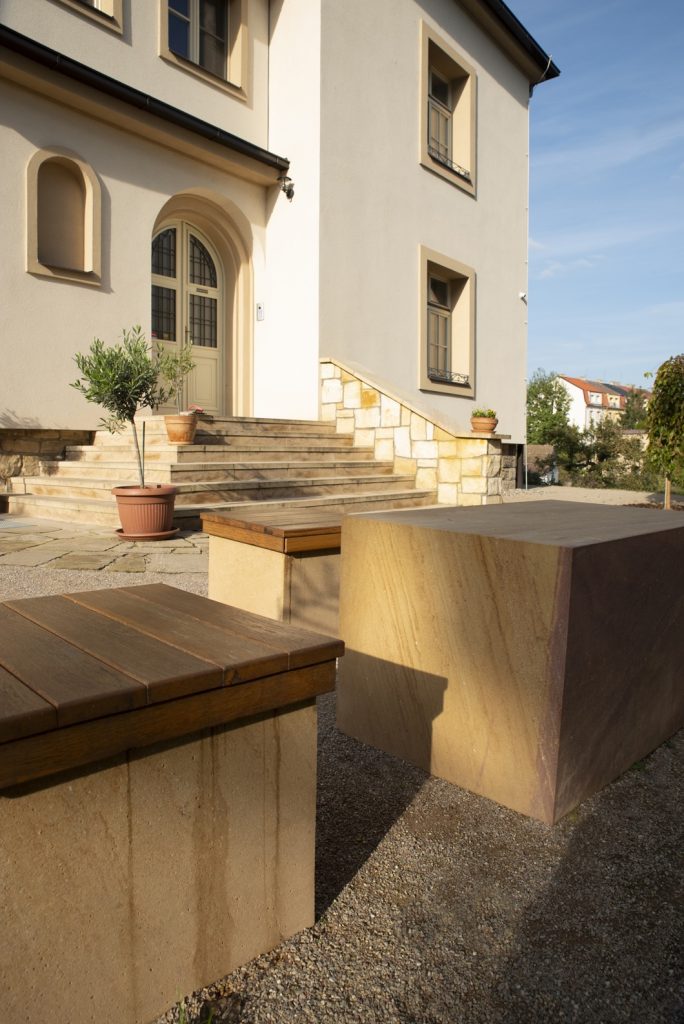 Fara Radotín Lavice z pískovce z lomu Vyhnánov v kombinaci s dřevěným sedákem tvoří esteticky vyvážené a přírodní posezení, které harmonicky doplňuje okolí fary.