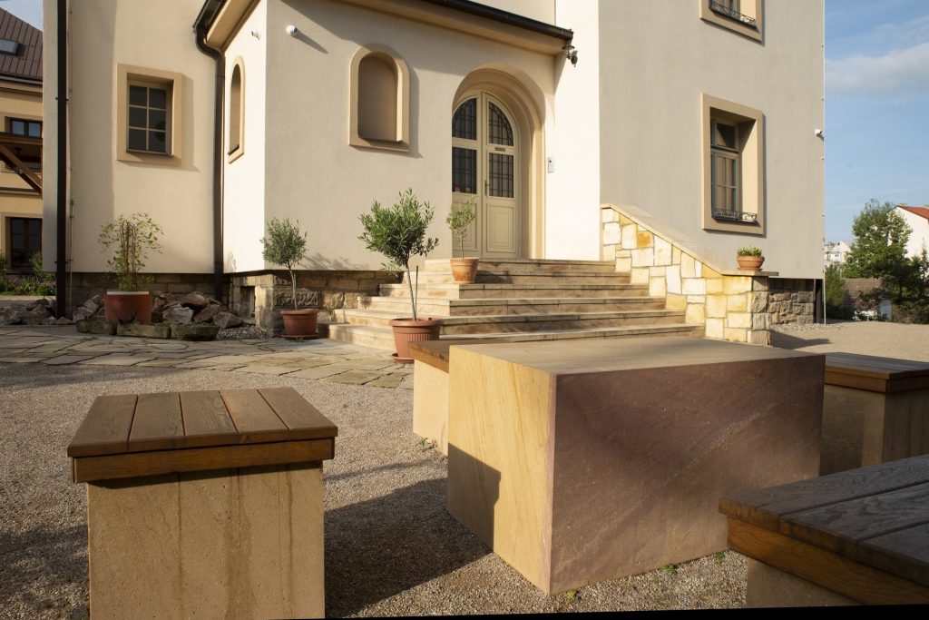 Fara Radotín Venkovní posezení s kamenným stolem z pískovce krásně ladí se schodištěm, zdí a dlažbou ze stejného materiálu.